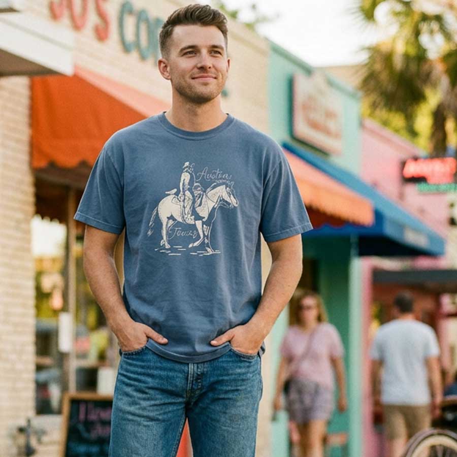 Man wearing a denim t-shirt with Austin Texas western inspired artwork, standing in front of a colorful storefront.