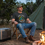 Model wearing the Dark Grey Camp More Worry Less graphic tee at a wooded campsite.