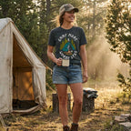 Model wearing the Dark Grey Camp More Worry Less graphic tee at a wooded campsite.