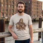 Man wearing a Dust Catch of the Day Walleye Tee beside an urban waterfront, with the Bigfoot fishing design visible.