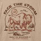 Close-up of a beige fabric surface with a distressed brown graphic print featuring a bison, the words “FACE THE STORM,” and smaller text reading “BUILT TO WEATHER IT” and “LOST DRAW PROVISIONS.”.