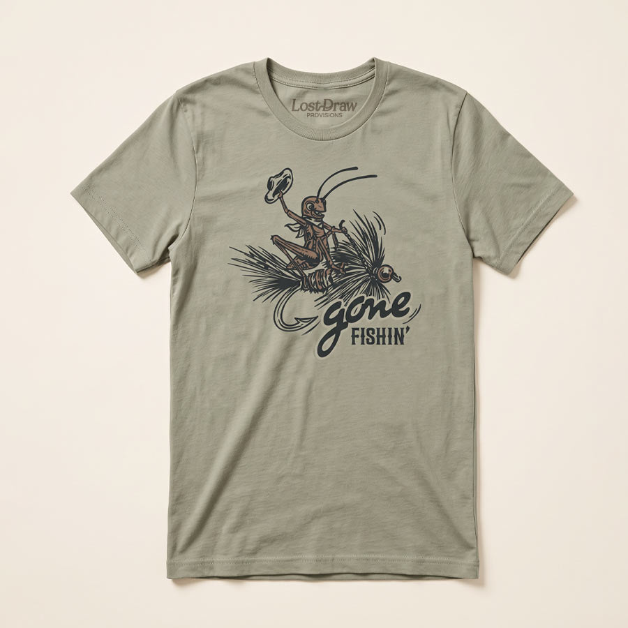 An thyme green short-sleeve t-shirt with a vintage-style graphic of a fly fisherman and the text 'gone FISHIN''. The brand 'Lost Draw' is printed inside the collar.