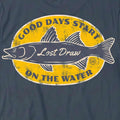 Close-up of the On the Water Tee's distressed yellow fishing badge and cream fish details on Vintage Navy fabric.