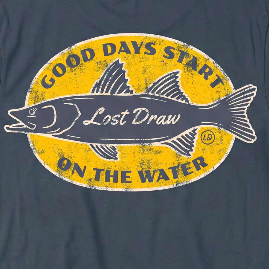 Close-up of the On the Water Tee's distressed yellow fishing badge and cream fish details on Vintage Navy fabric.