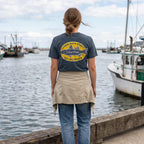 Woman wearing the On the Water Jersey Tee beside a Great Lakes harbor, displaying the vintage fishing graphic on the back.