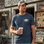 Man wearing the On the Water Jersey Tee outside a bait shop, displaying the small Lost Draw Provisions chest logo.