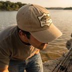 Man wearing a beige cap with a fish logo and 'Austin' text by a lake.