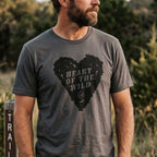 A man wearing a dark gray crewneck t-shirt with a distressed black heart graphic that reads 'HEART OF THE WILD' and a small circular 'LP' logo, set against a blurred outdoor background.