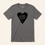 A dark gray crewneck t-shirt by LastDraw, featuring a black heart-shaped graphic on the chest with the text 'HEART OF THE WILD' and a small bear logo. The t-shirt is displayed flat against a light beige background.