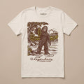 The Legendary Fishing Guide Tee in Vintage White featuring a vintage Bigfoot illustration holding a fish in a scenic river landscape.