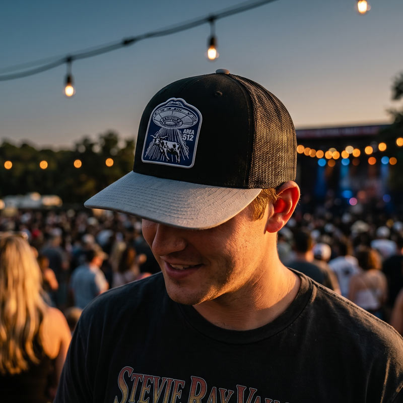Man wearing a cap with a logo at a concert with a crowd and lights in the background