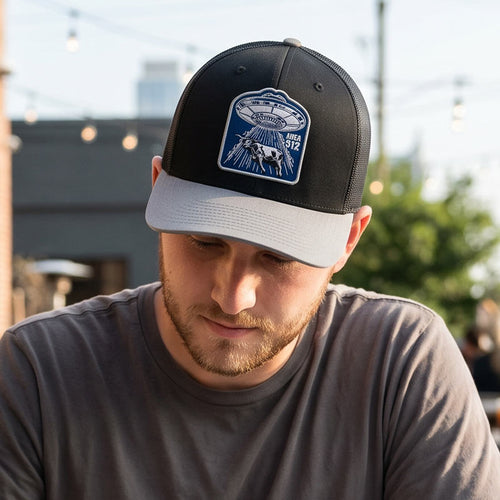 Man wearing a black and gray cap with a logo, looking down outdoors.