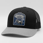 Black and gray cap with a UFO and cow patch on a light gray background