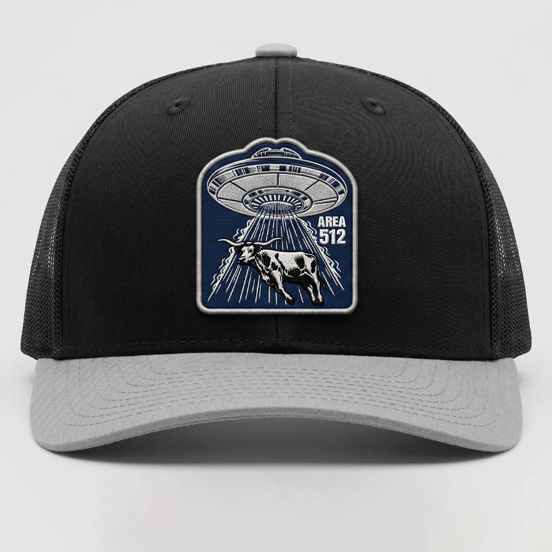 Black and gray cap with UFO and cow design on a light gray background