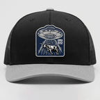 Black and gray cap with UFO and cow design on a light gray background