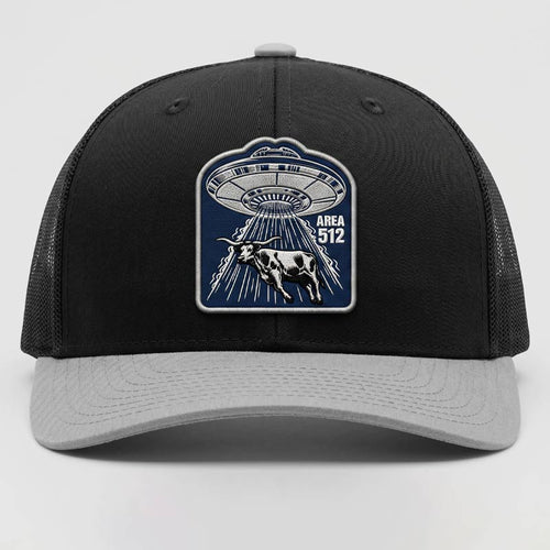 Black and gray cap with UFO and cow design on a light gray background