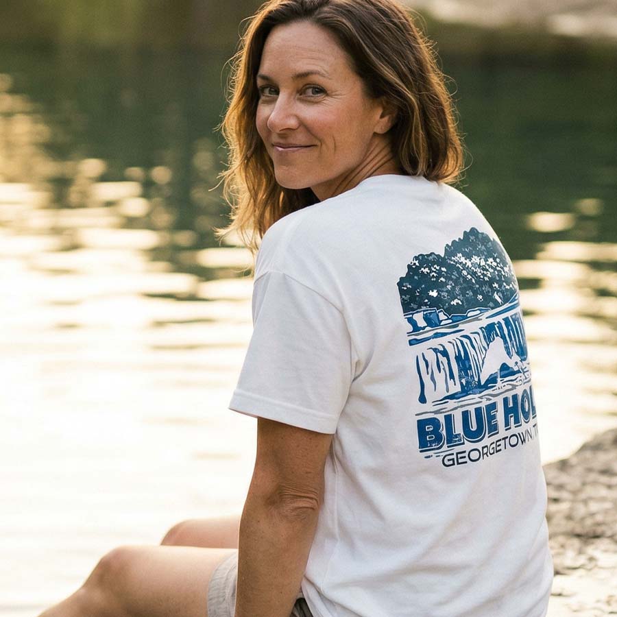 Woman wearing a Heavyweight oversized white graphic tee Blue Hole Georgetown TX lifestyle, sitting by a body of water.