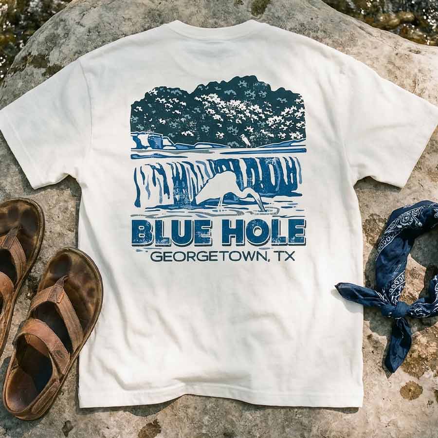 Heavyweight oversized white graphic tee Blue Hole Georgetown TX on a stone surface with sandals and a bandana.