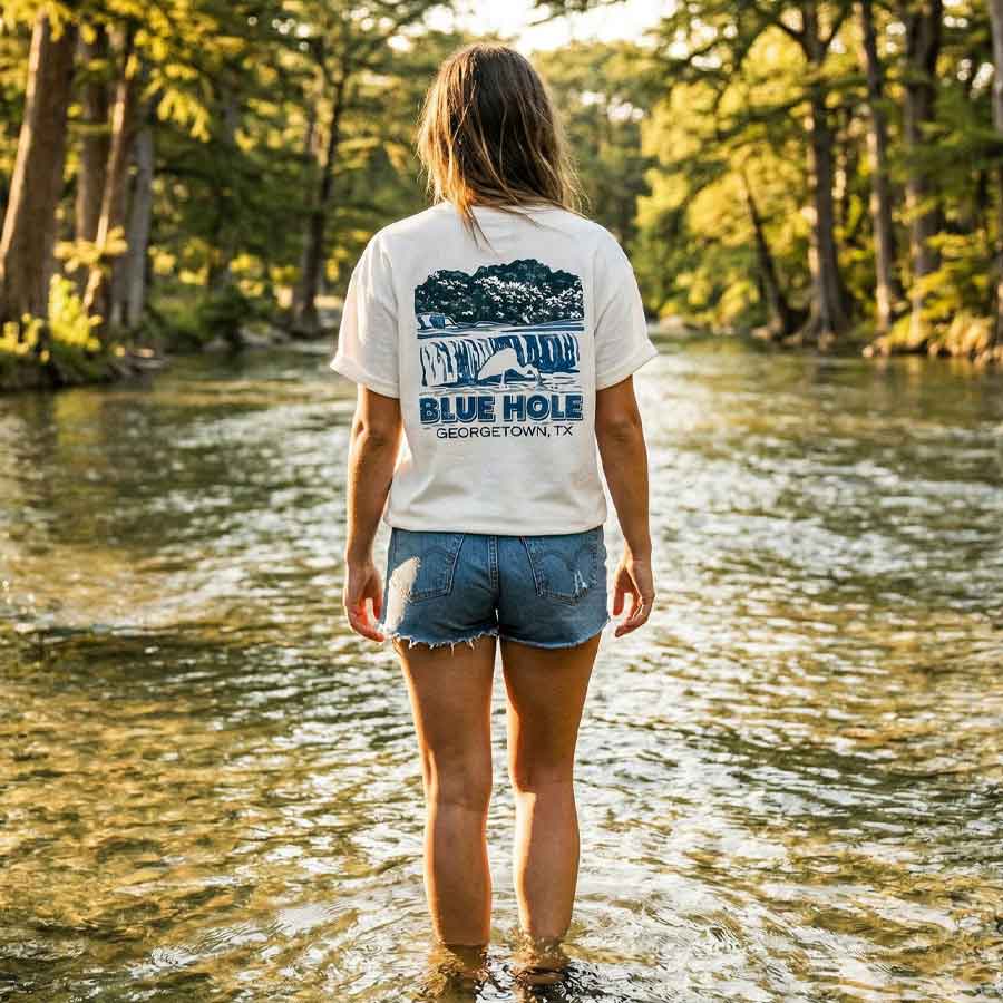 Woman wearing Heavyweight oversized white graphic tee Blue Hole Georgetown TX, standing in a river with trees in the background