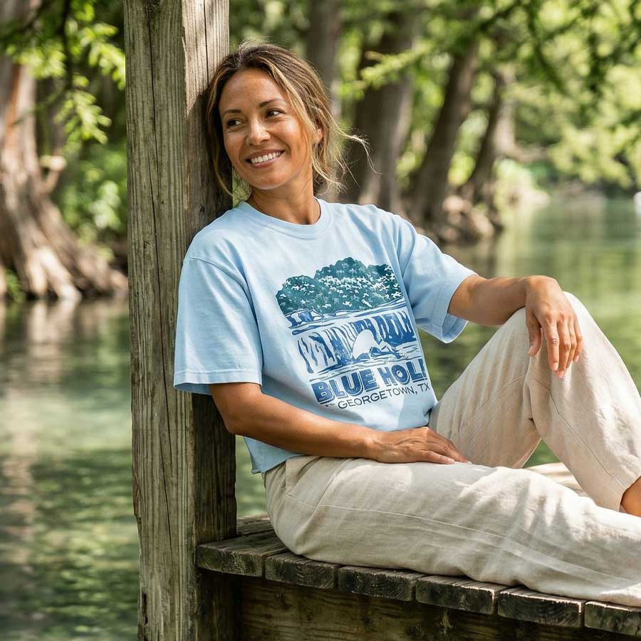 Woman sitting by a body of water wearing Blue Hole Georgetown Texas women’s boxy t-shirt garment-dyed white graphic tee