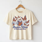 Butterfly Skies women’s boxy t-shirt with monarch butterflies and Austin skyline tee on a hanger against a white background