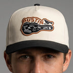 Beige cap with 'Austin, TX' logo worn by a person on a gray background