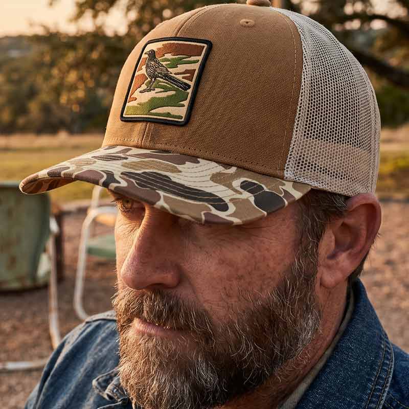 Man wearing a brown and camouflage cap with a patch outdoors