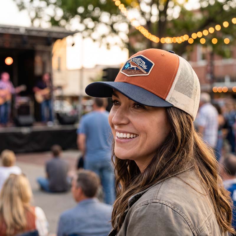 Woman wearing a baseball cap with a patch, smiling at an outdoor event.