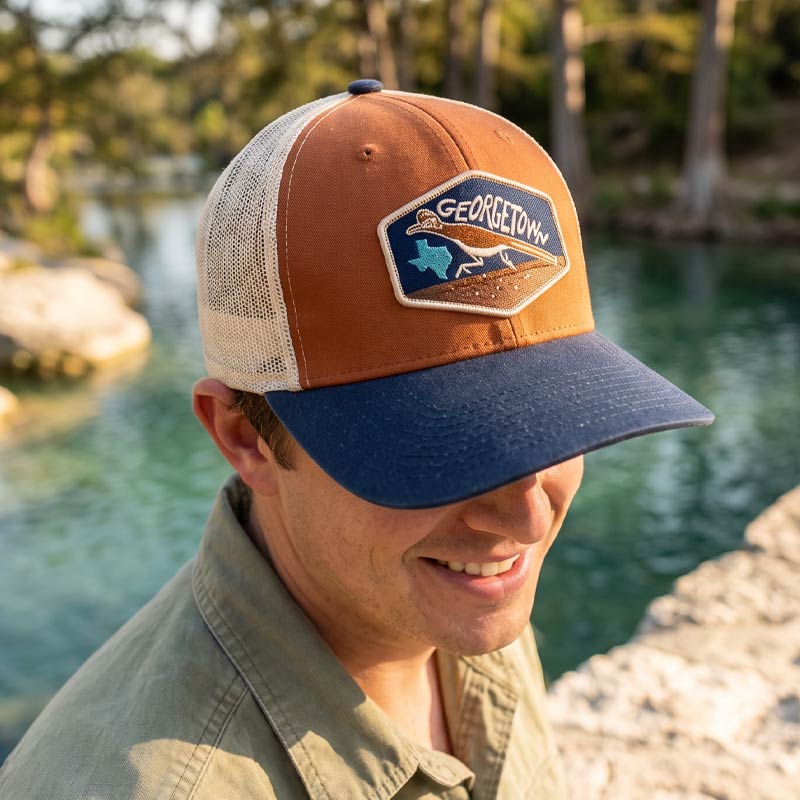 Man wearing a Georgetown cap by a body of water with trees in the background