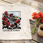 Texas wildflower bird graphic tee women’s cropped boxy t shirt on a wooden surface with flowers and a mug.