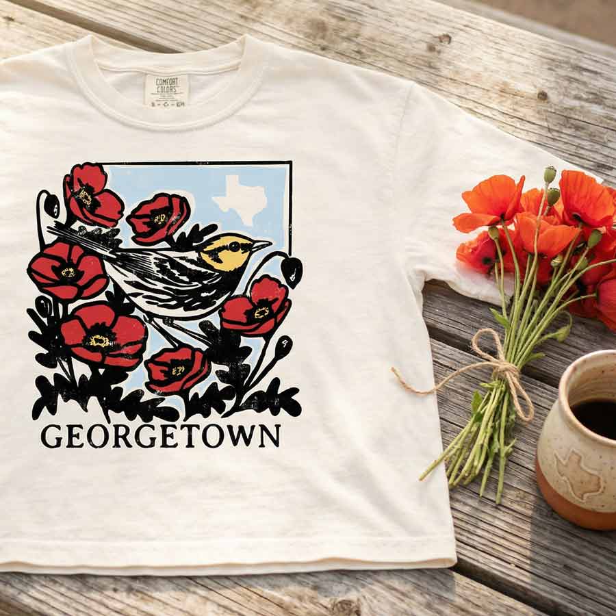 Texas wildflower bird graphic tee women’s cropped boxy t shirt on a wooden surface with flowers and a mug.