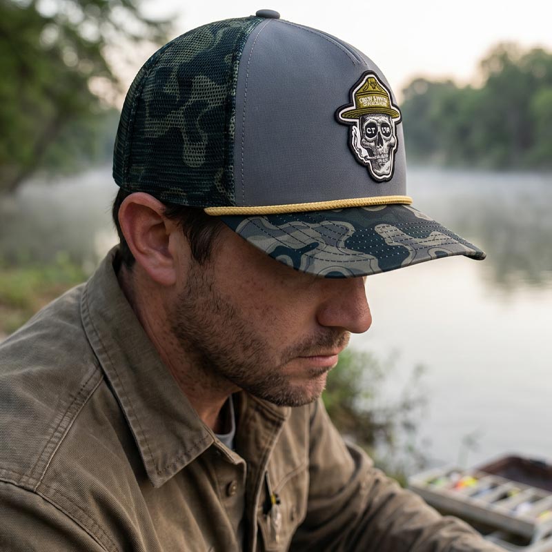 Man wearing a cap with a skull design by a body of water