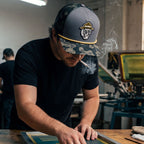 Man wearing a cap with a skull design, smoking a cigarette in a workshop.