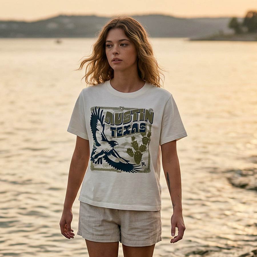 Lifestyle image of woman wearing relaxed fit boxy tee with hawk design walking near Lake Travis