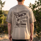 A man viewed from behind wearing a beige t-shirt with a large black graphic print on the back featuring an eagle, cowboy, and the text 'MORNINGBIRD AIRLINES' and 'COWBOYS FLY FREE AUSTIN, TEXAS'.