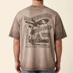 A man wearing a faded brown t-shirt, viewed from the back. The shirt features a large graphic print with the words 'MOCKINGBIRD AIRLINES', 'TEXAS STATE', 'AUSTIN, TEXAS', and 'COWBOYS FLY FREE' alongside an eagle and cowboy illustration.