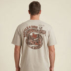 Man wearing a beige t-shirt with a snake and Texas flag graphic on the back against a beige background