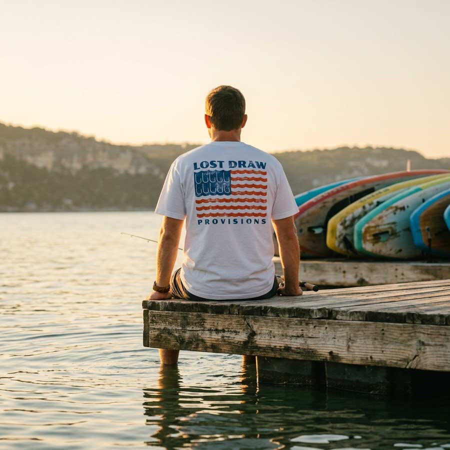 Person sitting on a dock wearing American flag fishing hook t-shirt river wave graphic oversized cotton tee