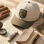 Putty and olive Lost Draw Provisions performance hat on a wooden surface with map, knife, and notebook.