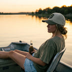 Person sitting on a boat holding a bottle, with a sunset over water in the background
