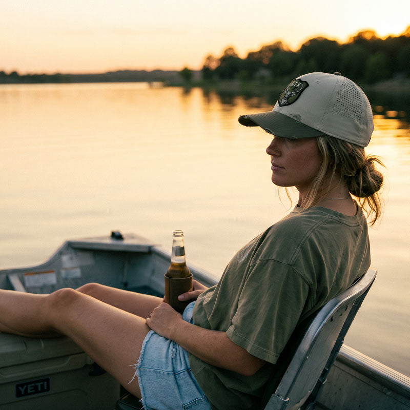 Person sitting on a boat holding a bottle, with a sunset over water in the background