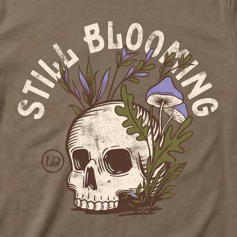 Close-up of the Still Blooming Tee's distressed cream skull, lavender mushrooms, and olive green botanical artwork on Vintage Brown fabric.