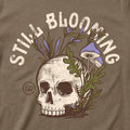 Close-up of the Still Blooming Tee's distressed cream skull, lavender mushrooms, and olive green botanical artwork on Vintage Brown fabric.