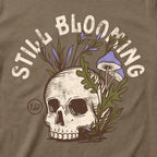 Close-up of the Still Blooming Tee's distressed cream skull, lavender mushrooms, and olive green botanical artwork on Vintage Brown fabric.