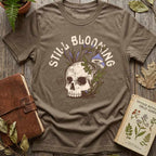 Vintage Brown Still Blooming graphic tee displayed with a potted fern, botanical book, and leather journal.
