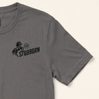 A close-up of a dark gray crewneck t-shirt featuring a black graphic print on the left chest with a rearing horse, a circular 'LP' logo, and the word 'STUBBORN'.